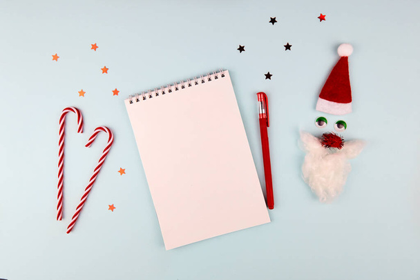 Christmas composition, wish list concept. Notebook with pen, Santa Claus with red hat and beard on light blue background. Flat lay, top view. - Photo, Image