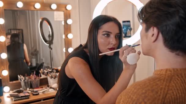 Makijaż studio - makijaż artysta stosujący szminkę na ustach męskiej modelki za pomocą pędzla - Materiał filmowy, wideo
