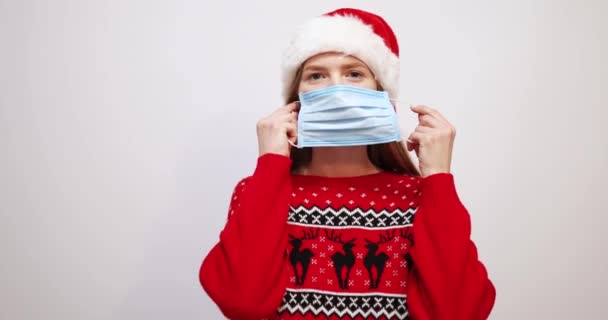  young woman wearing santa claus christmas hat, wearing medical protective mask, over white background - Séquence, vidéo