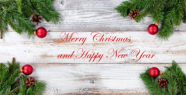 Рождественские вечнозеленые ветки и красные шарики украшения во всех углах на белом винтажном дереве плюс текстовое сообщение  - Фото, изображение
