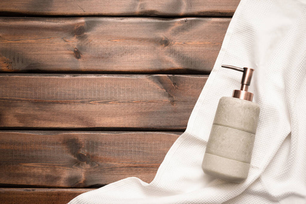 Soap dispenser bottle and towel on the brown wooden table background. - Foto, Imagem