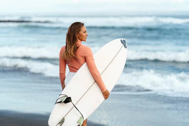 Young attractive surfer woman with white board at sunset on the ocean. Bali Indonesia. - Photo, image