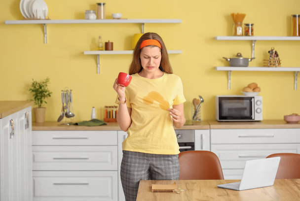 Наголошена молода жінка з кавовими плямами на футболці на кухні
 - Фото, зображення