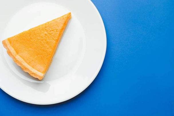 Тарелка с ломтиком вкусного тыквенного пирога на цветном фоне - Фото, изображение