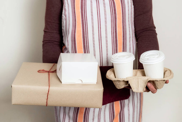 Deliver holding paper boxes and container take away with two white cups of coffee. - Photo, Image