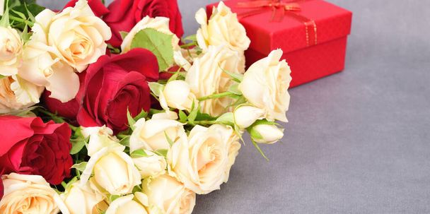 Oldalnézet egy hazug csokor vörös és fehér rózsa. Van egy kissé elmosódott ajándékdoboz a háttérben.. - Fotó, kép