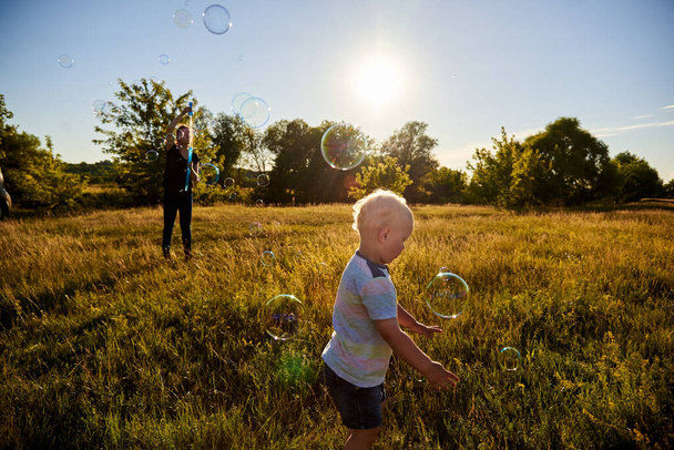 Mom and baby blow soap bubbles on a sunny meadow in summer, summer fun, selective focus. - Fotografie, Obrázek
