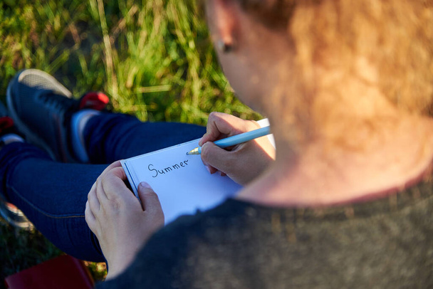 Kobieta zrobiła napis Lato na notatniku na trawie w naturze. - Zdjęcie, obraz