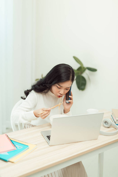 Confiado sonriendo atractiva joven mujer asiática empresario teniendo descanso para comer mientras está sentado en el escritorio de la oficina y el uso de teléfono móvil - Foto, imagen