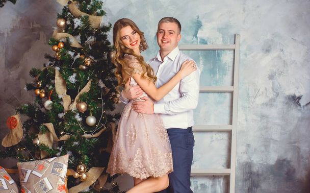 New year holiday portrait of a man and woman surprising him with a Christmas gift. Couple celebrating Christmas together. Beautiful young couple is celebrating at cozy romantic place. - Фото, зображення