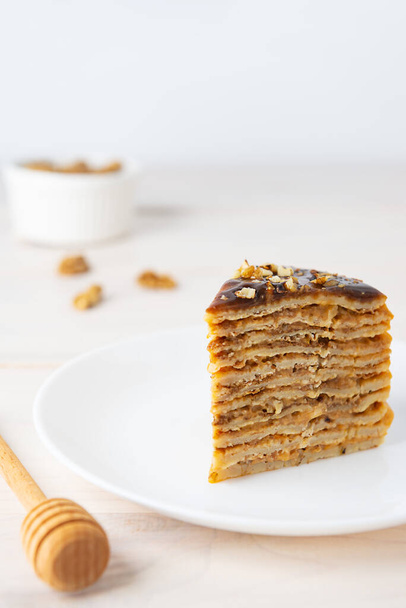 Slice of homemade pancake cake with chocolate caramel and walnuts on a white plate. Maslenitsa or Shrovetide. - Фото, изображение