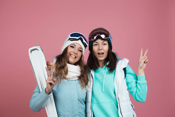 Two funny friends in winter clothes on a pink background. Two skiers - Foto, afbeelding