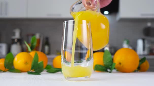 Zumo de naranja vertiendo en vidrio sobre mesa blanca - Imágenes, Vídeo