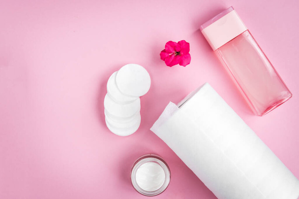 Face hygiene. Towel, tonic, cream, cotton pad and flower on pink background. - Photo, Image