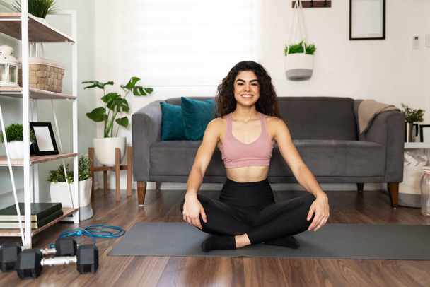 Jovem latina fazendo um exercício de ioga em sua sala de estar. Mulher hispânica sorrindo em uma pose fácil  - Foto, Imagem