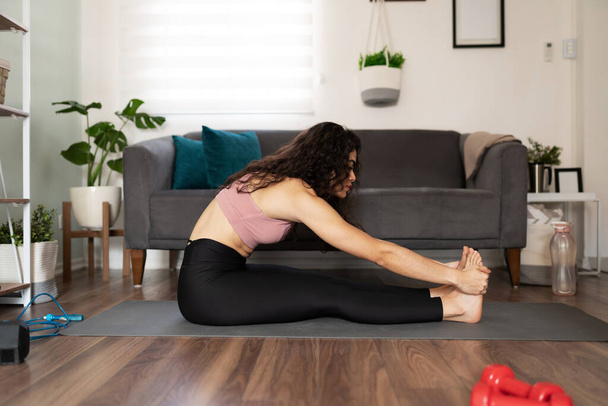 Actieve vrouw in de twintig die thuis traint. jonge hispanic vrouw oefenen in een voorwaarts buigen yoga pose - Foto, afbeelding