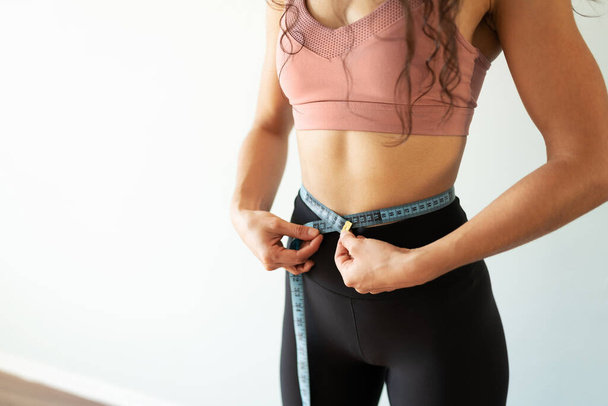 Close up of a strong and fit young woman measuring her waist for her weight loss goal  - Photo, image