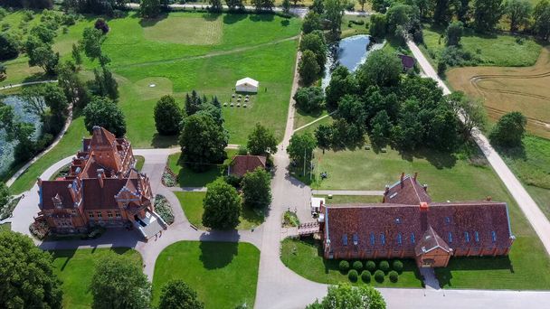 Jaunmoku Brick Medieval Castle Near Tukums, Latvia  at Pond With Fontain in Clear Sunny Summer Day From Above Top View. The Jaunmokas Manor Park. Aerial Dron 4k Shot - Photo, Image