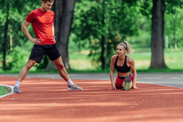 Young couple stretching before starting their morning jogging routine on a tartan track at the park. - Photo, Image