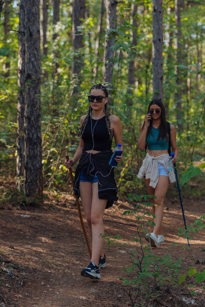 Sisters hiking through beautiful woods while wearing a backpack and enjoying nature. Female bonding. - Photo, Image