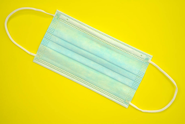 Antibakteriální lékařská maska modré barvy na žlutém pozadí. Koncept koronavirové ochrany. Kvalitní fotografie - Fotografie, Obrázek