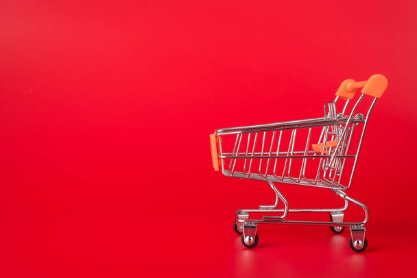 Shopping concept. Side profile close up photo of miniature shopping cart isolated on red background with copyspace - Photo, Image