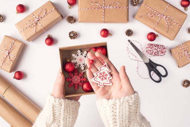 Pov felső fölött közelkép felső nézet fotó női kéz gazdaság bemutató doboz karácsonyi dekoráció bemutató lógó fa hópelyhek felett fehér munkahely - Fotó, kép