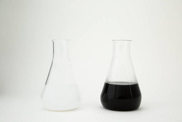 Wissenschaftliches Laborglas Erlenmeyerkolben gefüllt mit weißer und schwarzer Flüssigkeit auf weißem Hintergrund. - Foto, Bild