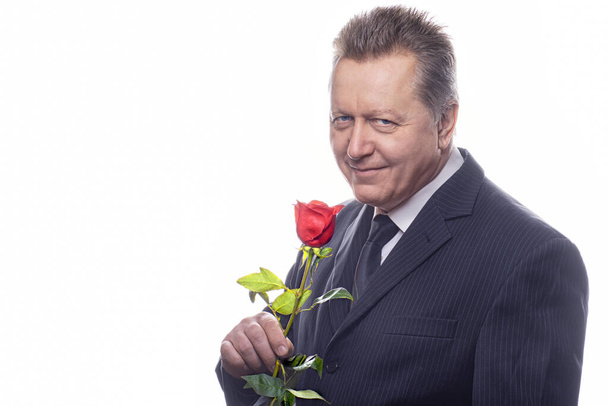 Романтичный старший джентльмен, держащий розу и смотрящий в камеру. Изолированный на белом фоне. - Фото, изображение