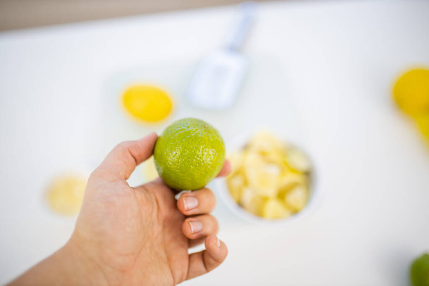 Main de femme tenant une lime au-dessus de tranches de citrons et de citrons - Photo, image