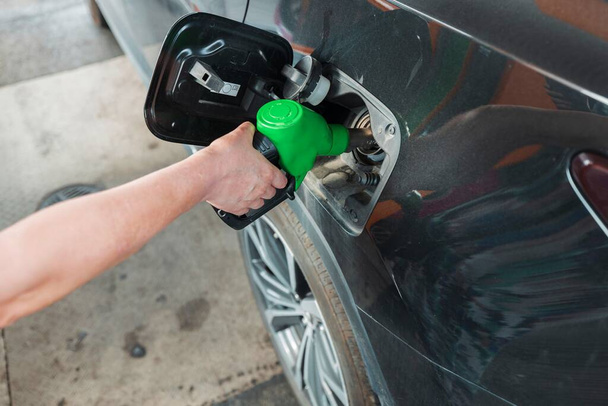 Γυναίκα ρίχνει καύσιμα στο ντεπόζιτο ενός μαύρου αυτοκινήτου στο βενζινάδικο. Σχέδιο μεταφοράς. Όμορφα φόντο. - Φωτογραφία, εικόνα