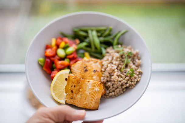 Hand holding salmon and buckwheat dish with green beans - Photo, Image