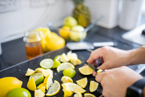 Férfi kéz citromot és lime-ot szeletel fekete tálcán - Fotó, kép