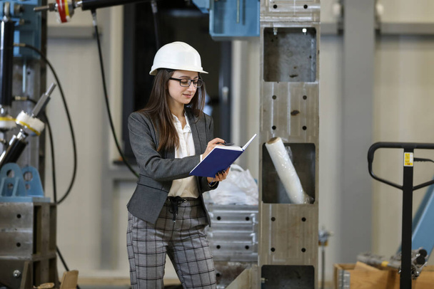 Portret van een vrouwelijke fabrieksmanager in een zakenpak met notitieboekje, die het werkproces tijdens de fabricage controleert - Foto, afbeelding