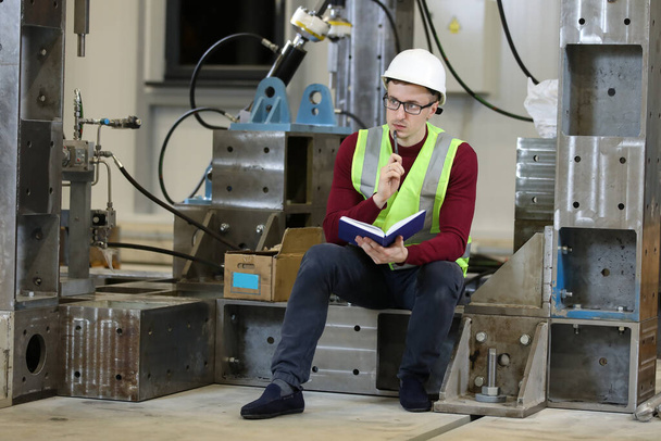 Retrato de um gerente de fábrica do sexo masculino em um chapéu duro branco e suéter vermelho Controlando o processo de trabalho no fabricante do helicóptero. - Foto, Imagem