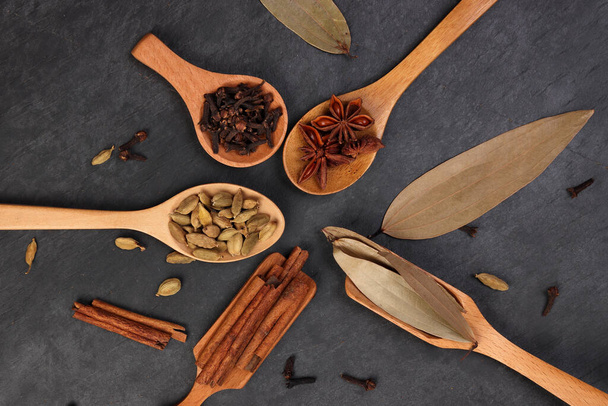 Mix variety spice cinnamon cardamom clove bay leaf wooden spoon scattered on black slate background - Photo, Image