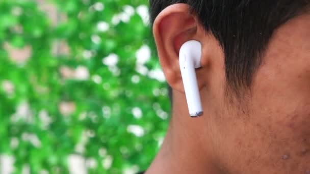 νεαρός άνδρας βάζοντας ασύρματο ακουστικό τηλέφωνο κοντά  - Πλάνα, βίντεο