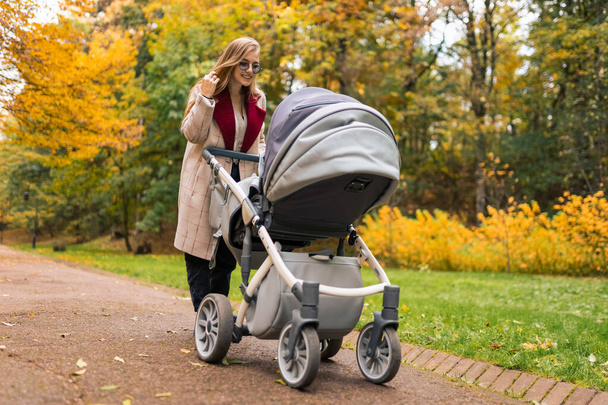 Wesoła matka z wózkiem spaceruje w jesiennym parku z dala od zgiełku miasta - Zdjęcie, obraz