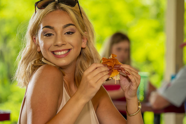 Ein hinreißendes junges blondes Model genießt ihr Mittagessen im Freien, während es während der Covid-19-Pandemie einen sicheren Abstand zu anderen hält - Foto, Bild