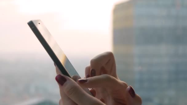 Close up side view - γυναικεία χέρια που χρησιμοποιούν συσκευή smartphone ενάντια στην προβολή του cityscape - Πλάνα, βίντεο