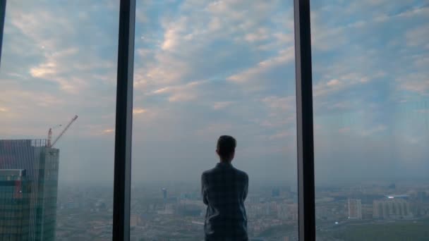 Widok z tyłu zamyślona kobieta patrząc na krajobraz miasta przez okno drapacza chmur - Materiał filmowy, wideo