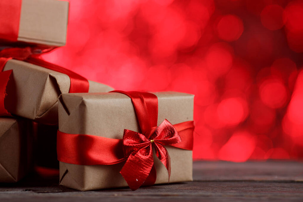Подарункова різдвяна коробка зі стрічкою на дерев'яному столі на абстрактному червоному тлі
. - Фото, зображення