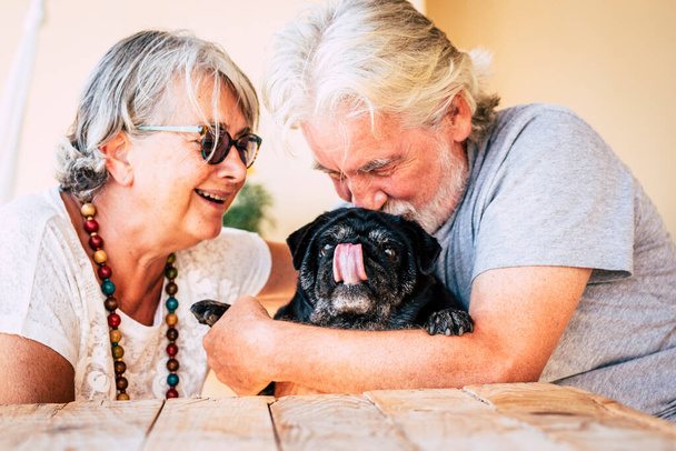 Fröhliches altes Seniorenpaar lächelt und genießt ihren besten Freund, den Hundemops, mit Liebe - Foto, Bild