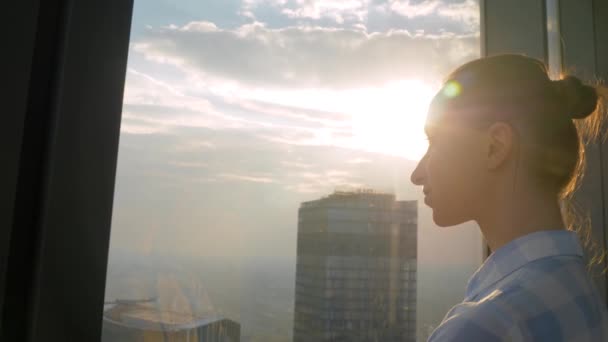 Portret van een vrouw die door het raam van de wolkenkrabber naar het stadsgezicht kijkt - Video