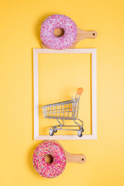 dos Donuts de color rosa con migas de pastelería de colores, sobre un fondo amarillo. el concepto de compras. foto vertical - Foto, imagen