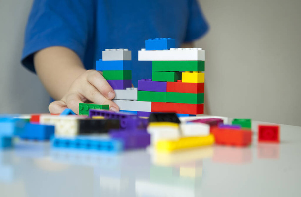 Close up of child's hands playing with colorful plastic bricks at the table. Toddler having fun and building out of bright bricks. Early learning. stripe background. Developing toys. - Photo, image