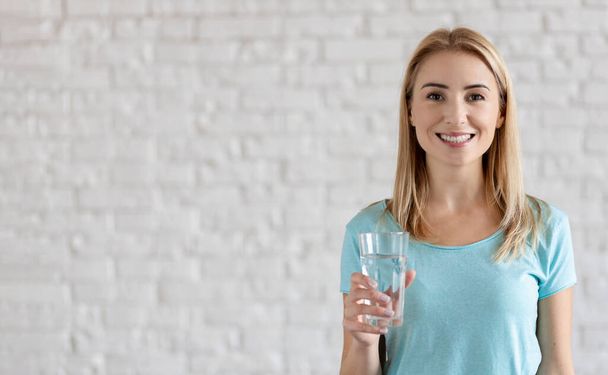 Portrait of happy smiling young woman with glass of fresh water. Healthy lifestyle concept - 写真・画像