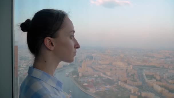 Portret van een dure vrouw die door het raam van de wolkenkrabber naar het stadsgezicht kijkt - Video