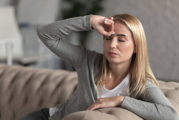 Young woman sat down on sofa at home, she suffers from headache - Foto, Imagen