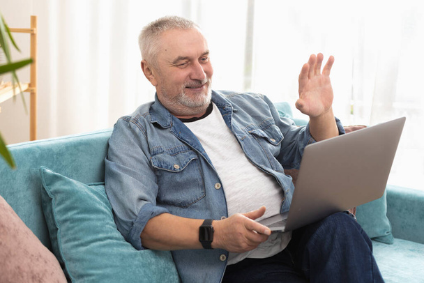 Gray-haired adult man smiles broadly, communicates online and greets interlocutors - Photo, Image